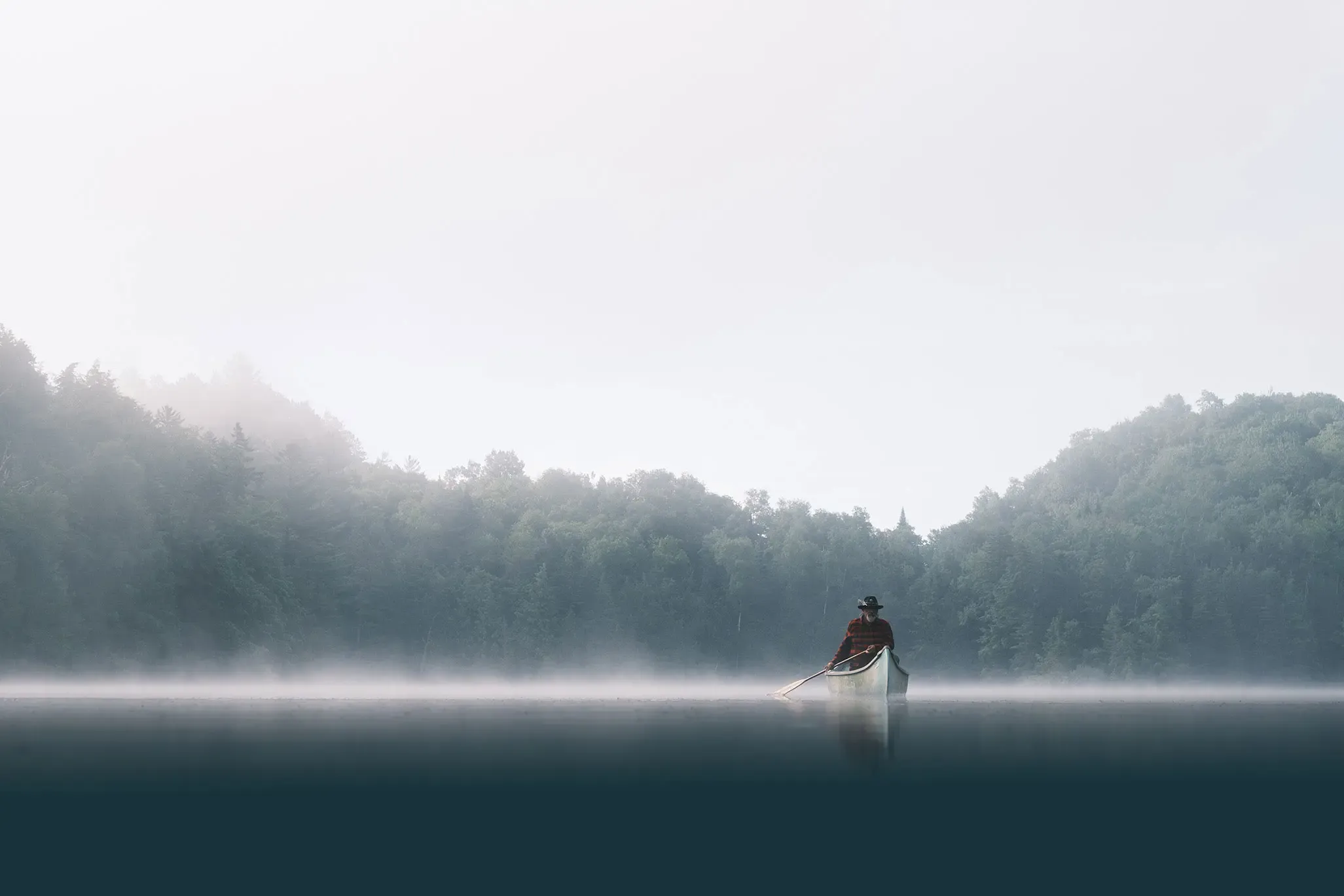 Un canot glissant sur un lac des Laurentides, au petit matin, dans la brume